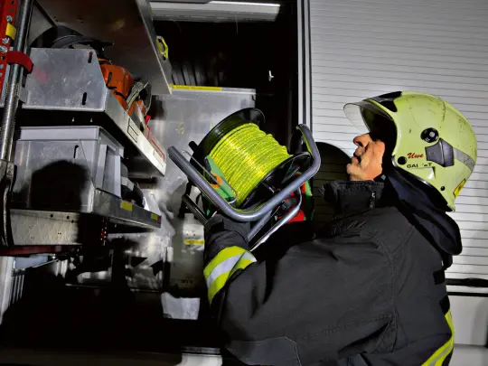 Feuerwehrmann hebt Kabeltrommel in Feuerwehrauto