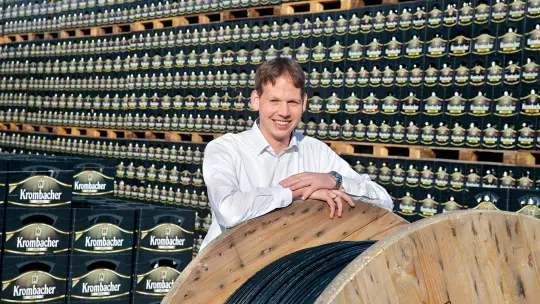 A man standing behind a big cable drum in a hall full of Krombacher beer 