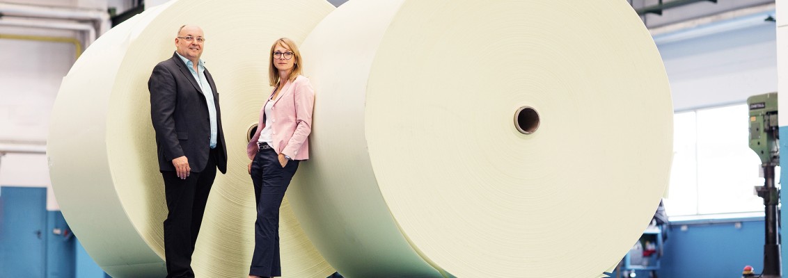 Two persons standing in front of big wrapped rolls